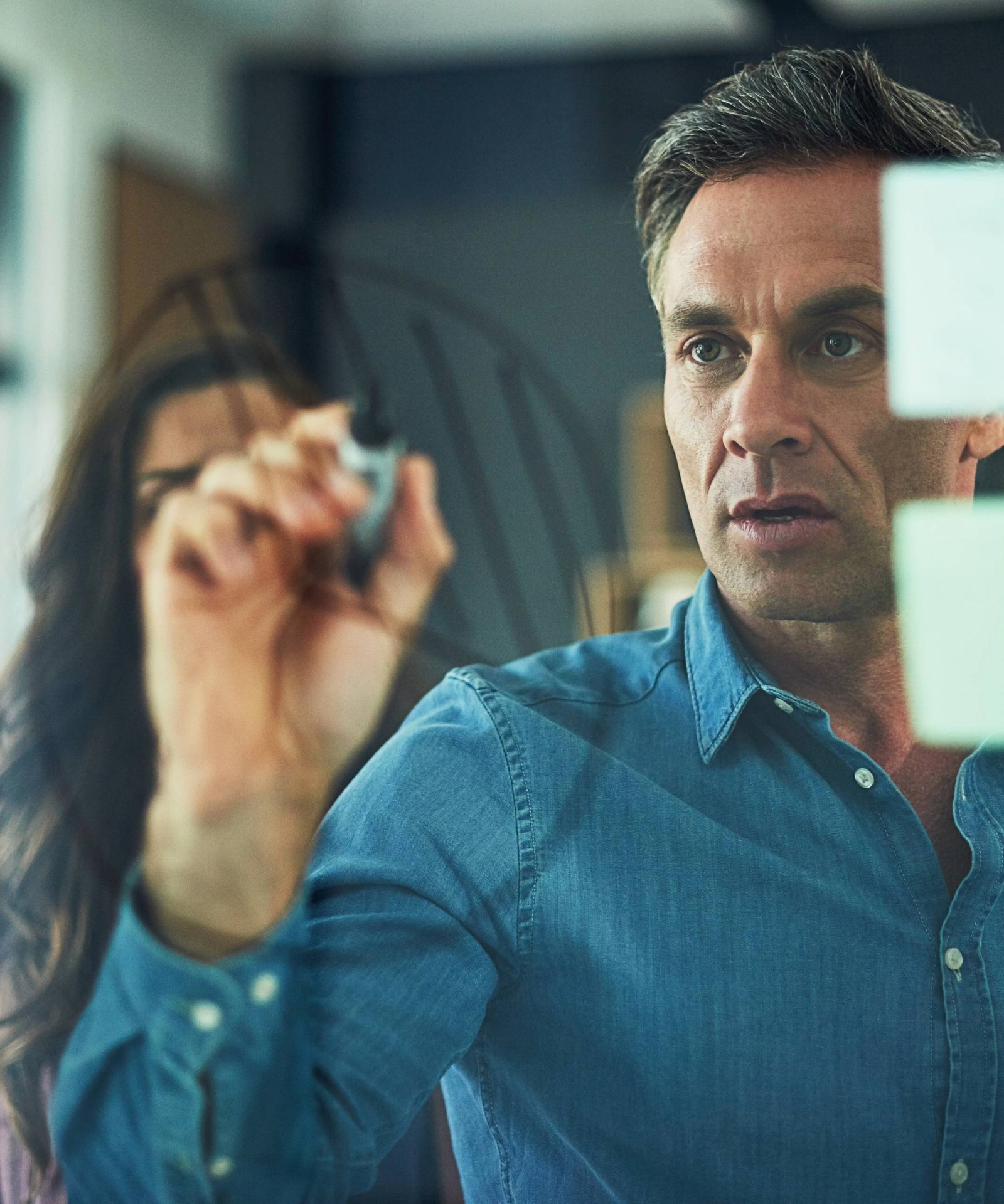 A man drawing on a glass wall with a marker